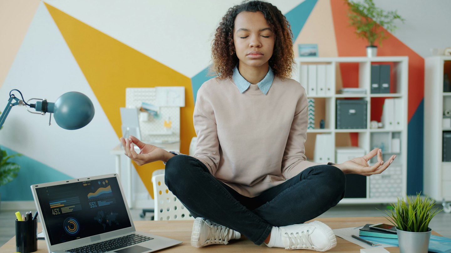 Woman meditating cross-legged on an office desk.