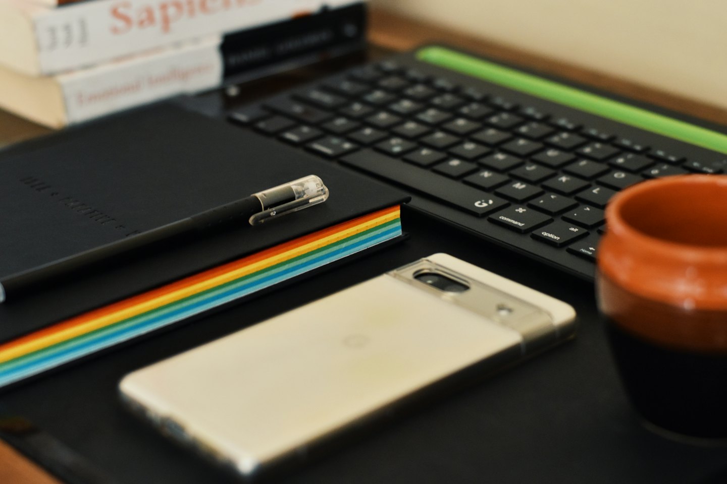 A notebook, pen, smartphone, and keyboard on a desk.