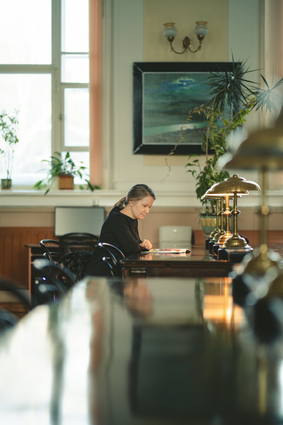 Woman reading a book at a dark wood table in a study.